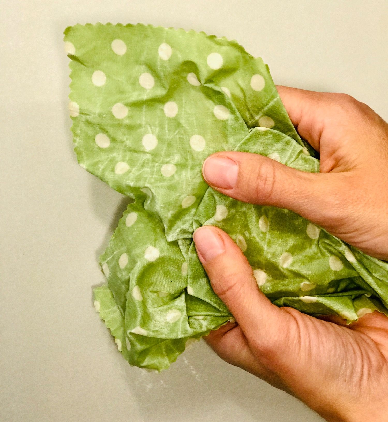 Eine Hand hält ein zerknittertes, grün mit weißen Punkten bedrucktes Bienenwachstuch.