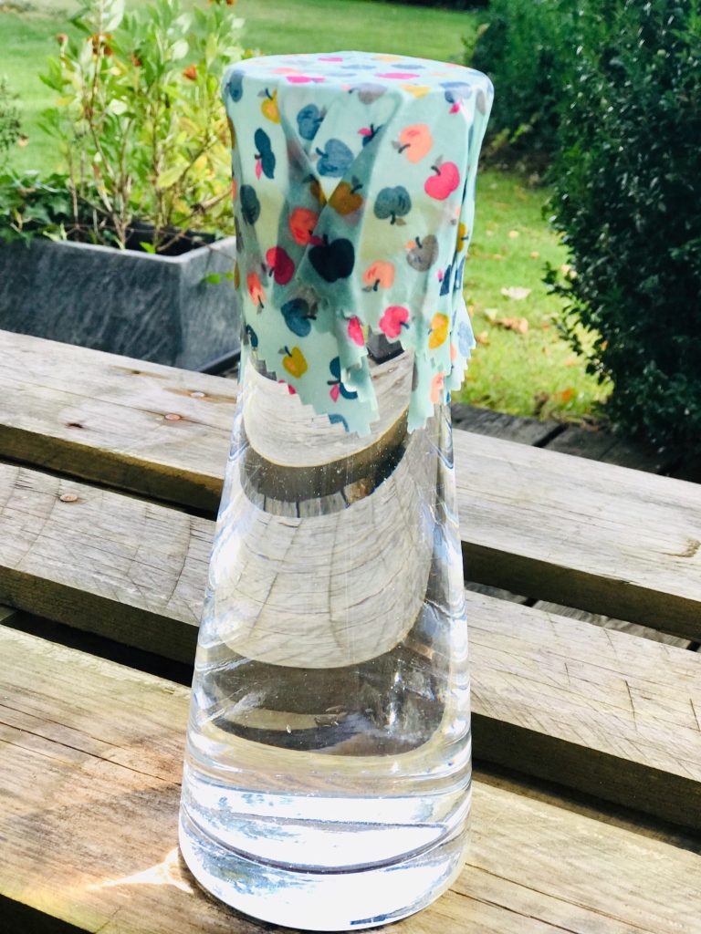 Ein Wasserkaraffe mit einem bunten, kleinen Bienenwachstuch abgedeckt.