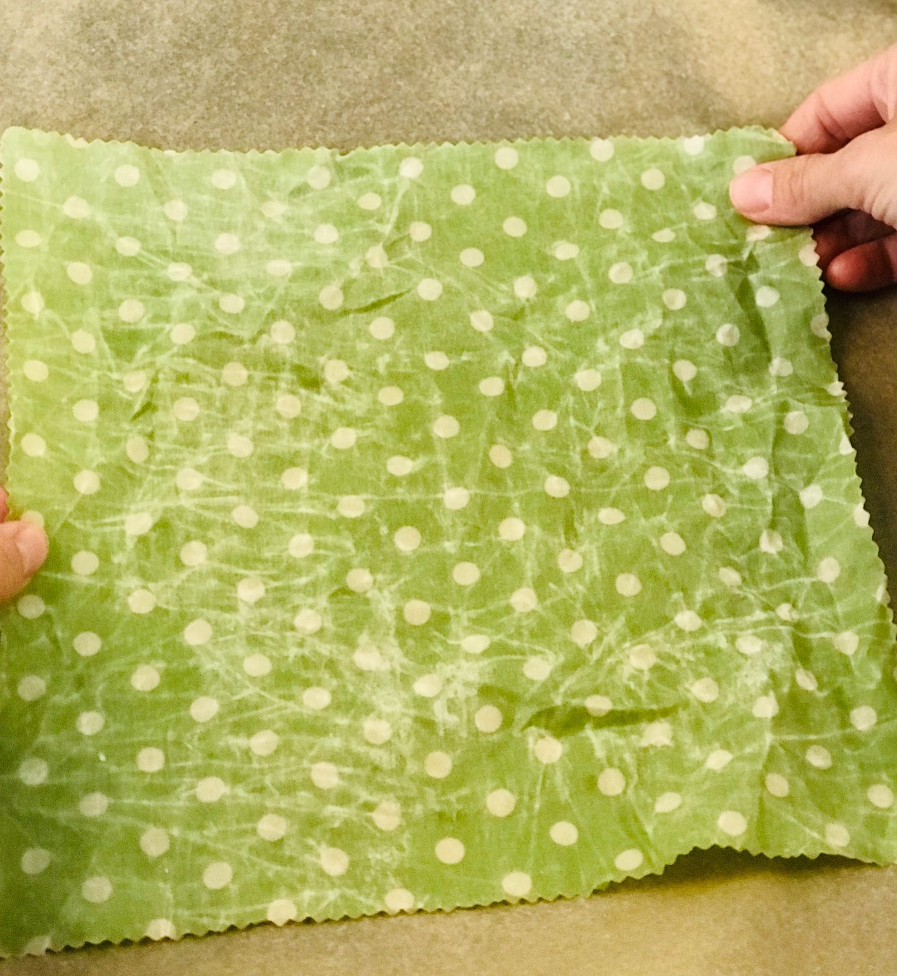 Grünes zerknittertes Wachstuch mit weißen Punkten wird aufs Backblech mit Backpapier gelegt.