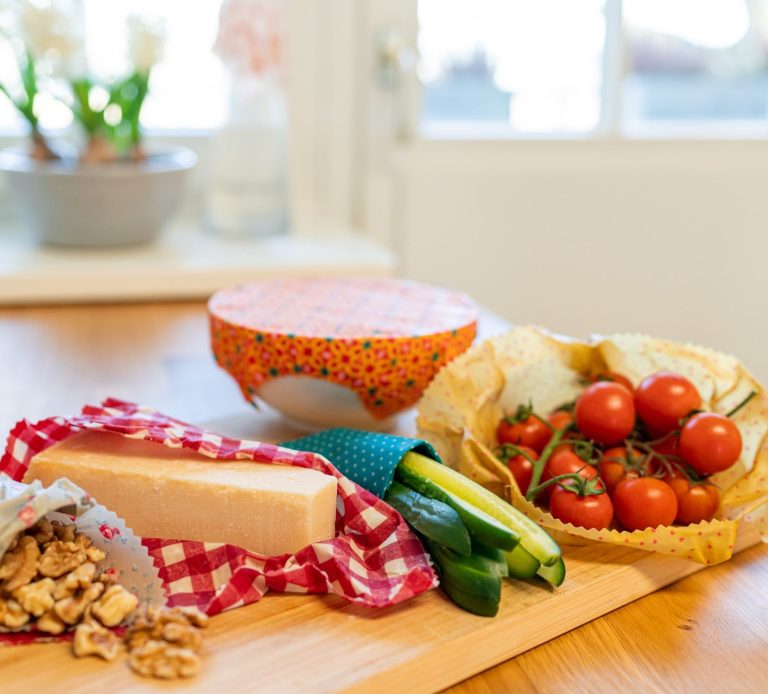 Zutaten auf einem Tisch: Käse, Tomaten, Zucchini und Nüsse in einer Schüssel. Alles in Bienenwachstüchern eingewickelt.