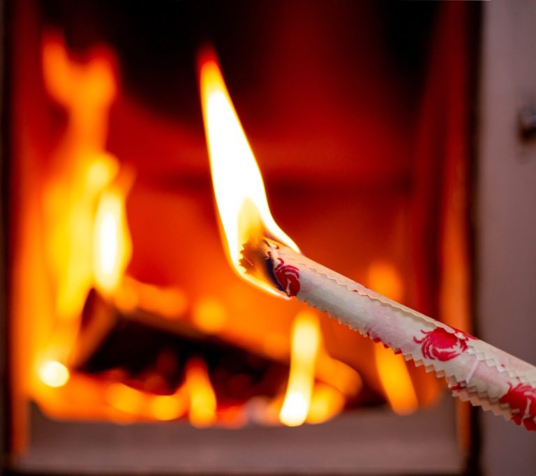 Ein brennendes zusammengerolltes Bienenwachstuch vor einem lodernden Kaminfeuer.