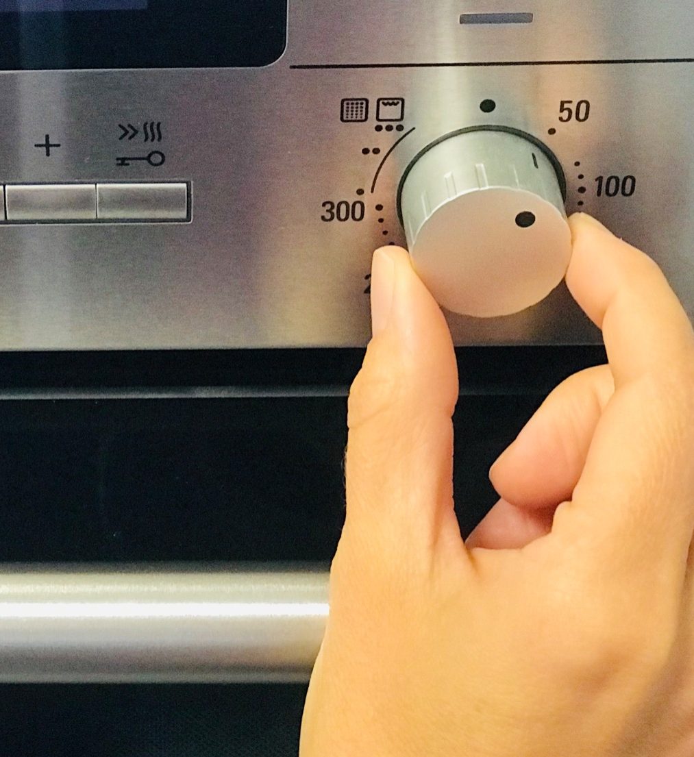Hand dreht einen Temperaturregler eines Ofens auf 50 Grad.