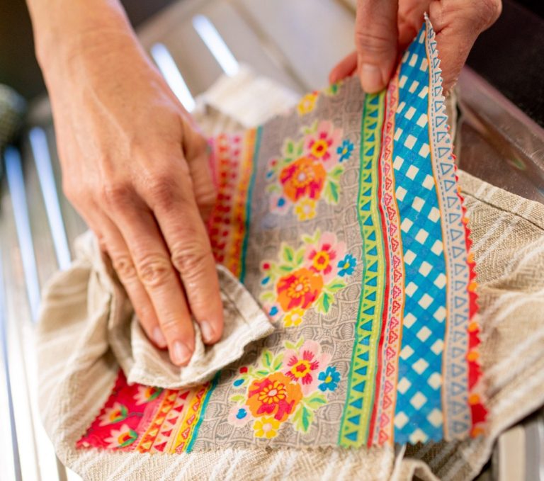 Eine Hand trocknet vorsichtig ein buntes Wachstuch mit einem Geschirrhandtuch.