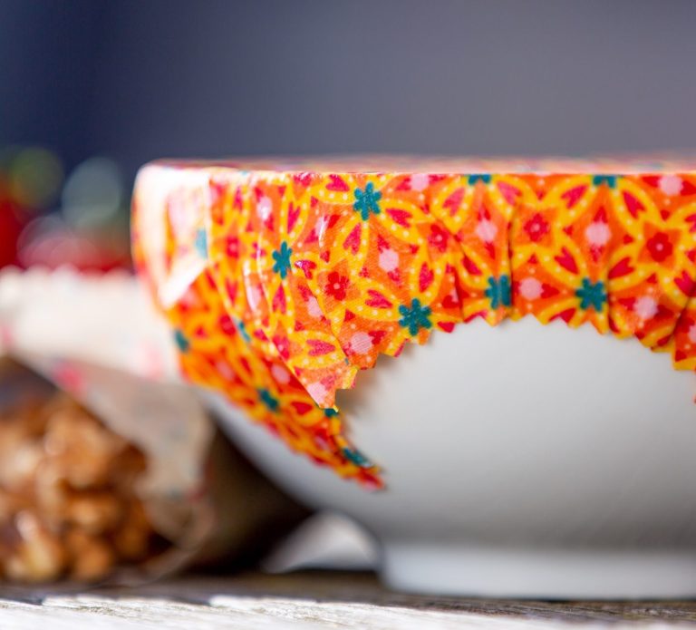 Weisse Schüssel mit lebendigem, buntem Bienenwachstuch abgedeckt.