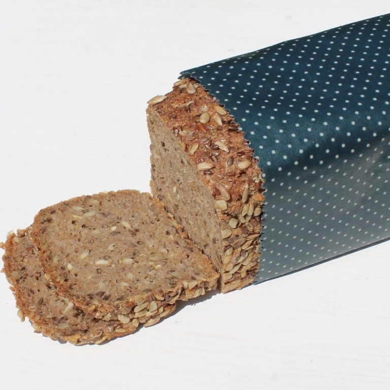 Vollkornbrot in einem großen, blauen, gepunkteten Bienenwachstuch mit zwei geschnittenen Scheiben.