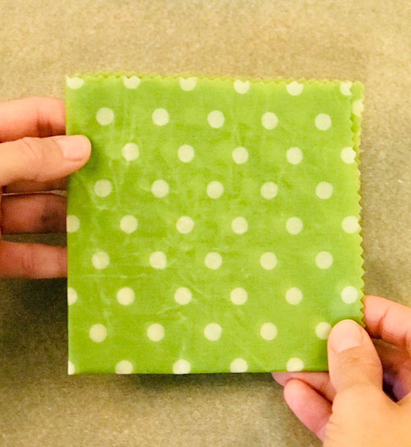 Grünes zusammengefaltetes Bienenwachstuch mit weißen Punkten, von zwei Händen gehalten.